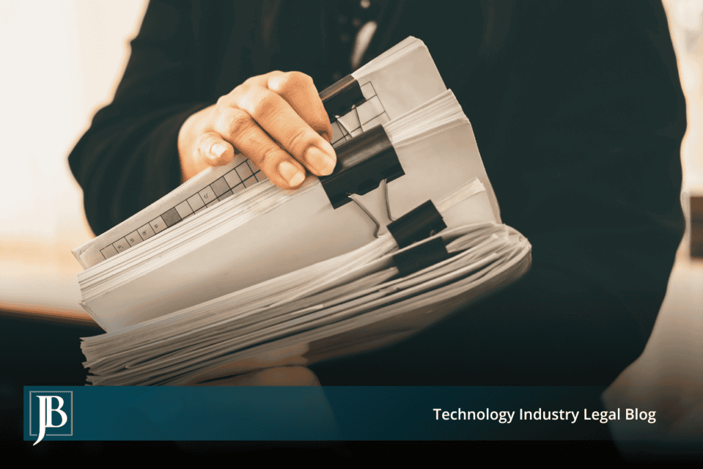 Person in a dark suit holding a thick stack of paper files secured with black binder clips, illustrating customer records a departing employee may take from a Florida business.