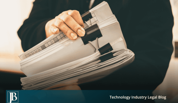 Person in a dark suit holding a thick stack of paper files secured with black binder clips, illustrating customer records a departing employee may take from a Florida business.