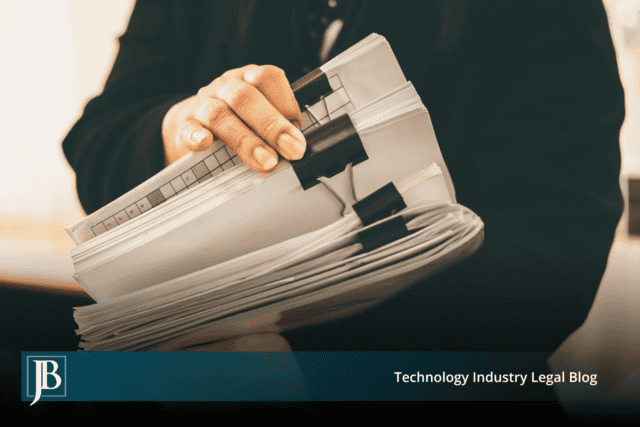 Person in a dark suit holding a thick stack of paper files secured with black binder clips, illustrating customer records a departing employee may take from a Florida business.