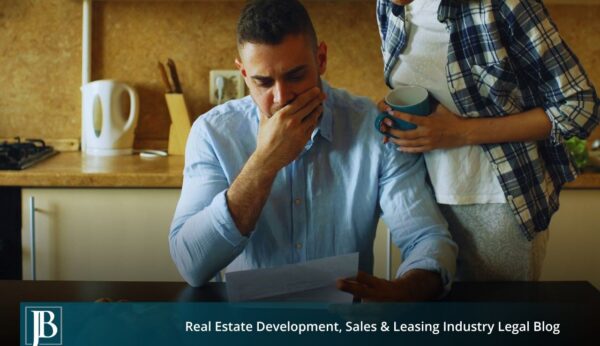 A worried man in a blue shirt reads a legal notice at his kitchen table while a woman holding a coffee mug stands beside him, below a Jimerson Birr banner reading "Real Estate Development, Sales & Leasing Industry Legal Blog."