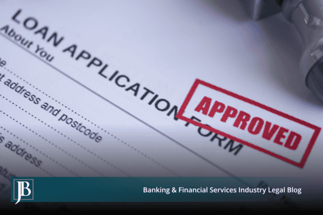 Close-up of a commercial loan application form stamped APPROVED in red ink, with a rubber stamp resting beside it.