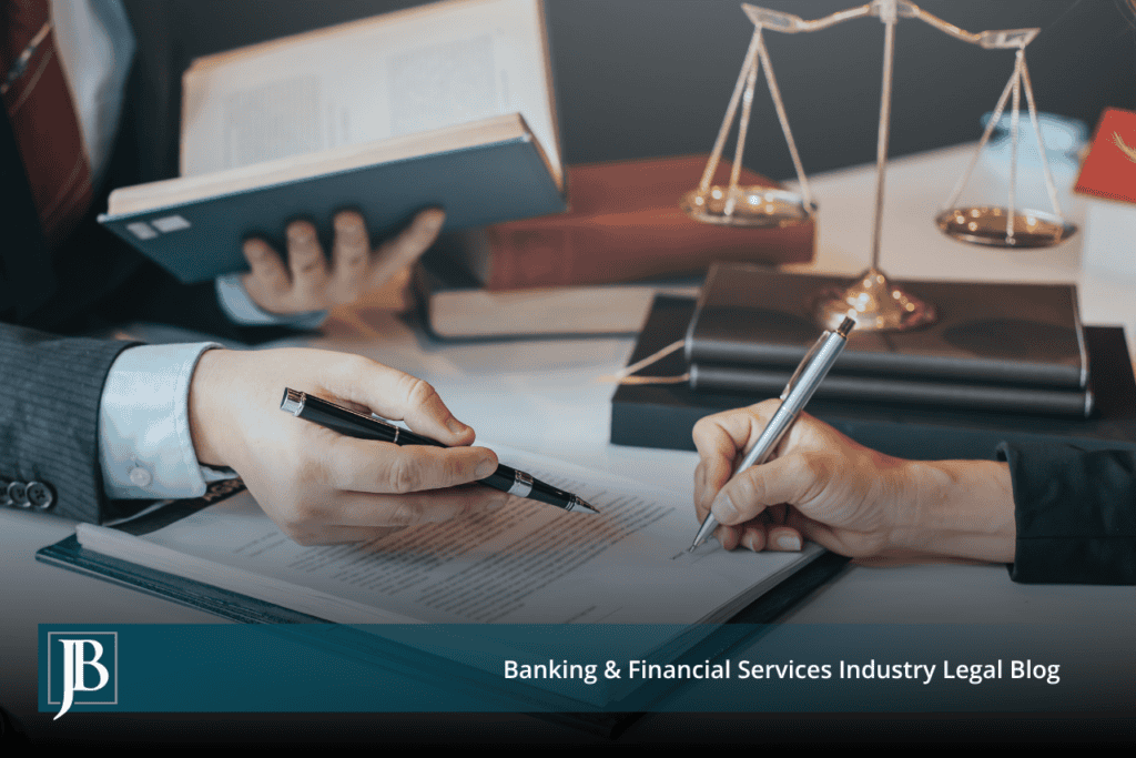 Two business attorneys seated at a desk reviewing and signing a commercial collection litigation defense agreement, with law books and gold scales of justice in the background, on the Jimerson Birr Banking and Financial Services Industry Legal Blog.