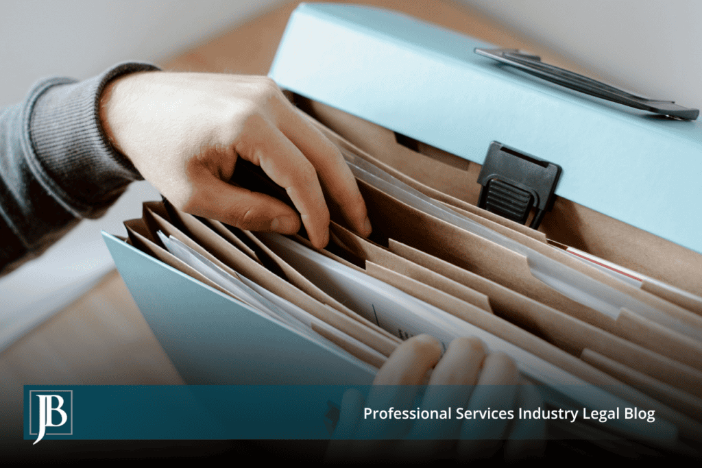 Hand pulling a file from an expanding folder of documents, illustrating document collection and production during discovery in business litigation.