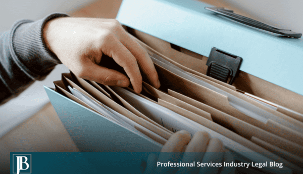 Hand pulling a file from an expanding folder of documents, illustrating document collection and production during discovery in business litigation.