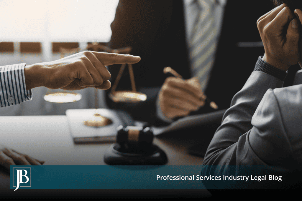 One businessperson points accusingly across a conference table at another while a lawyer sits behind a scale of justice and gavel, illustrating how business disputes turn into unfair competition lawsuits.