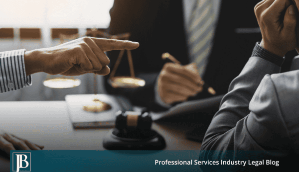 One businessperson points accusingly across a conference table at another while a lawyer sits behind a scale of justice and gavel, illustrating how business disputes turn into unfair competition lawsuits.