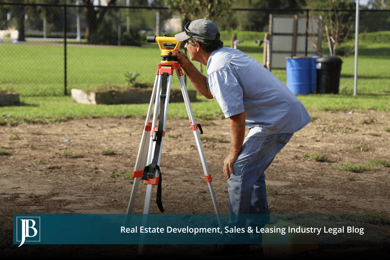 Surveyor sighting a level on a tripod at a fenced vacant lot, illustrating right-of-way work for US 41 through Inverness