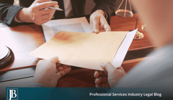 Business owner handing a manila envelope of documents across a desk to a lawyer during a first meeting.