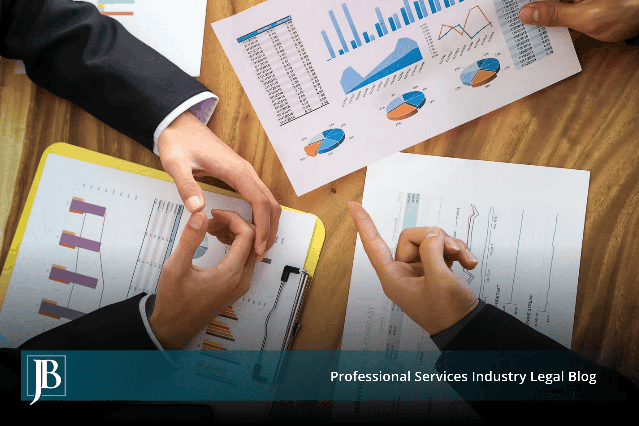 Overhead view of business professionals in suits pointing at printed financial charts and reports on a wooden conference table